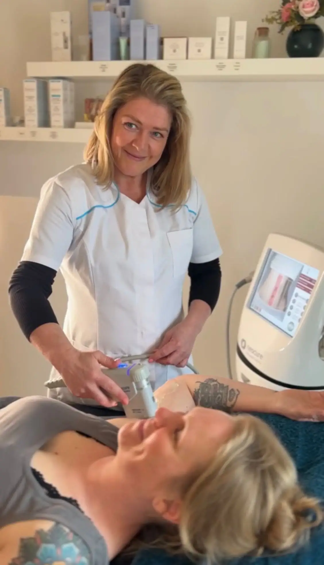Davina van Dionis behandelt een glimlachende cliënt met esthetisch apparaat in haar studio