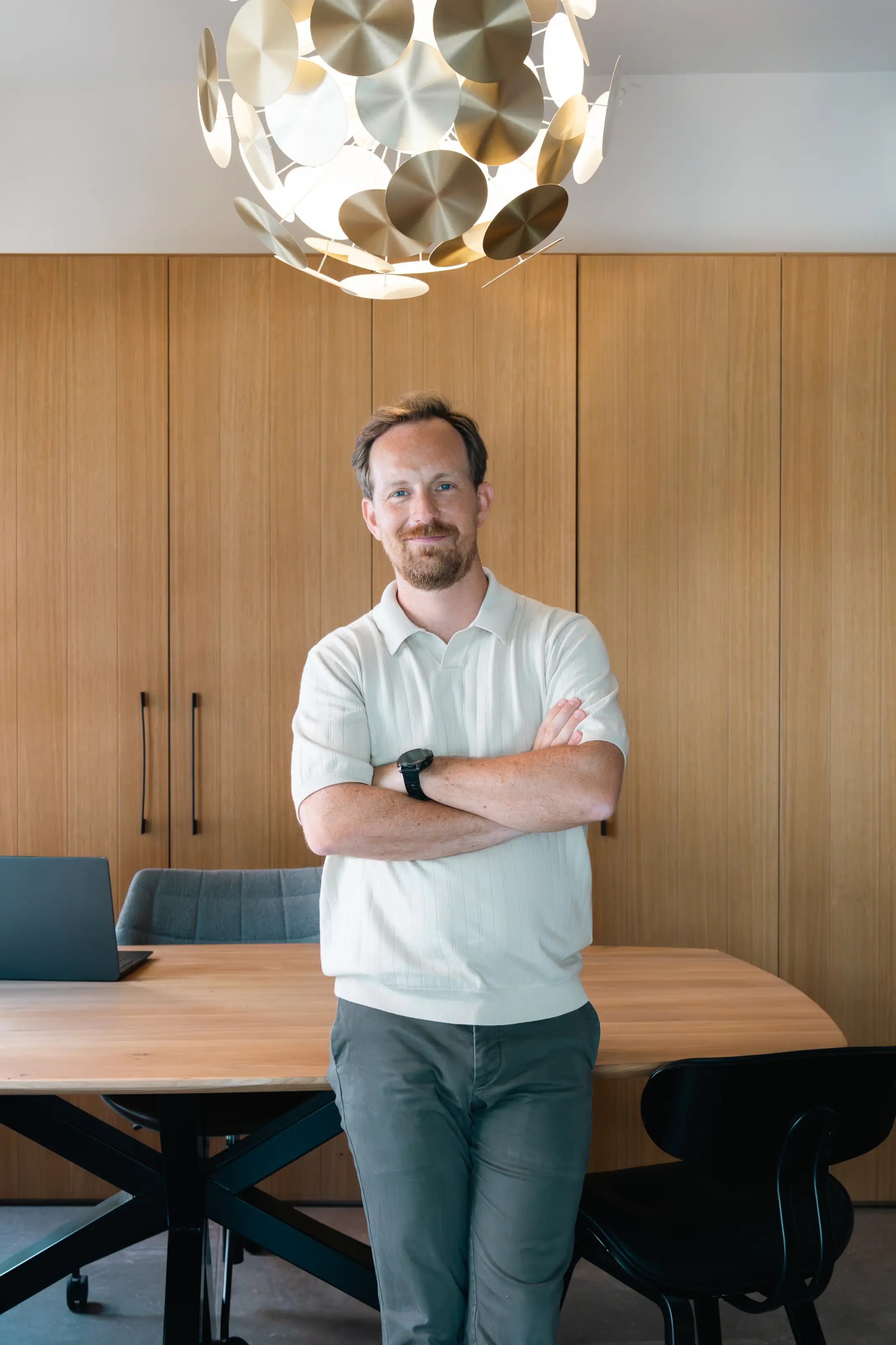 Tobias staat met gekruiste armen in zijn kantoor met houten wandpanelen