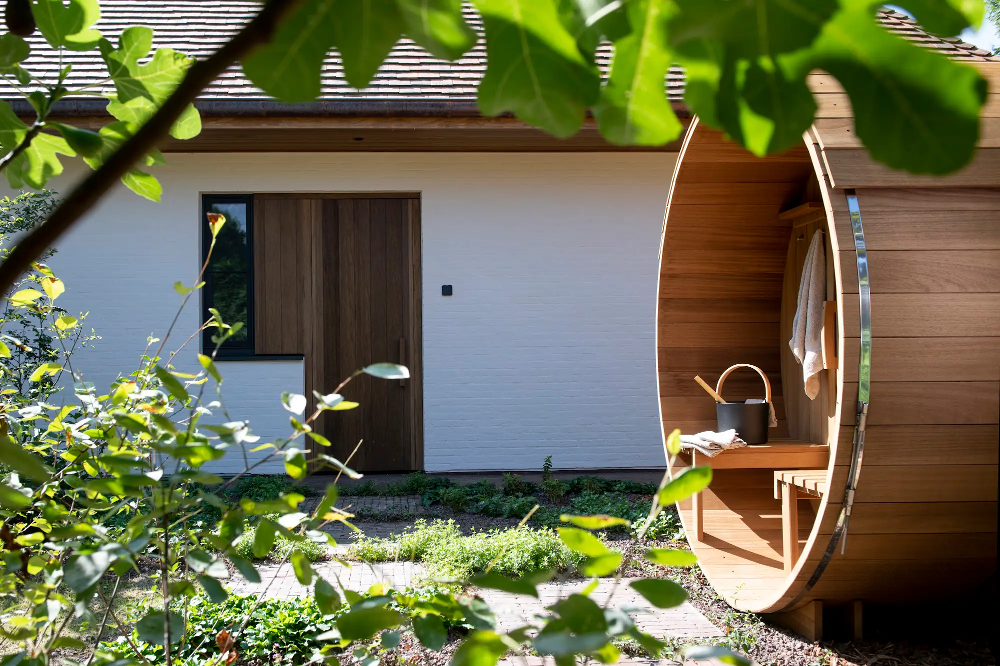Wit gebouw met houten deur naast de tonsauna, omringd door groen