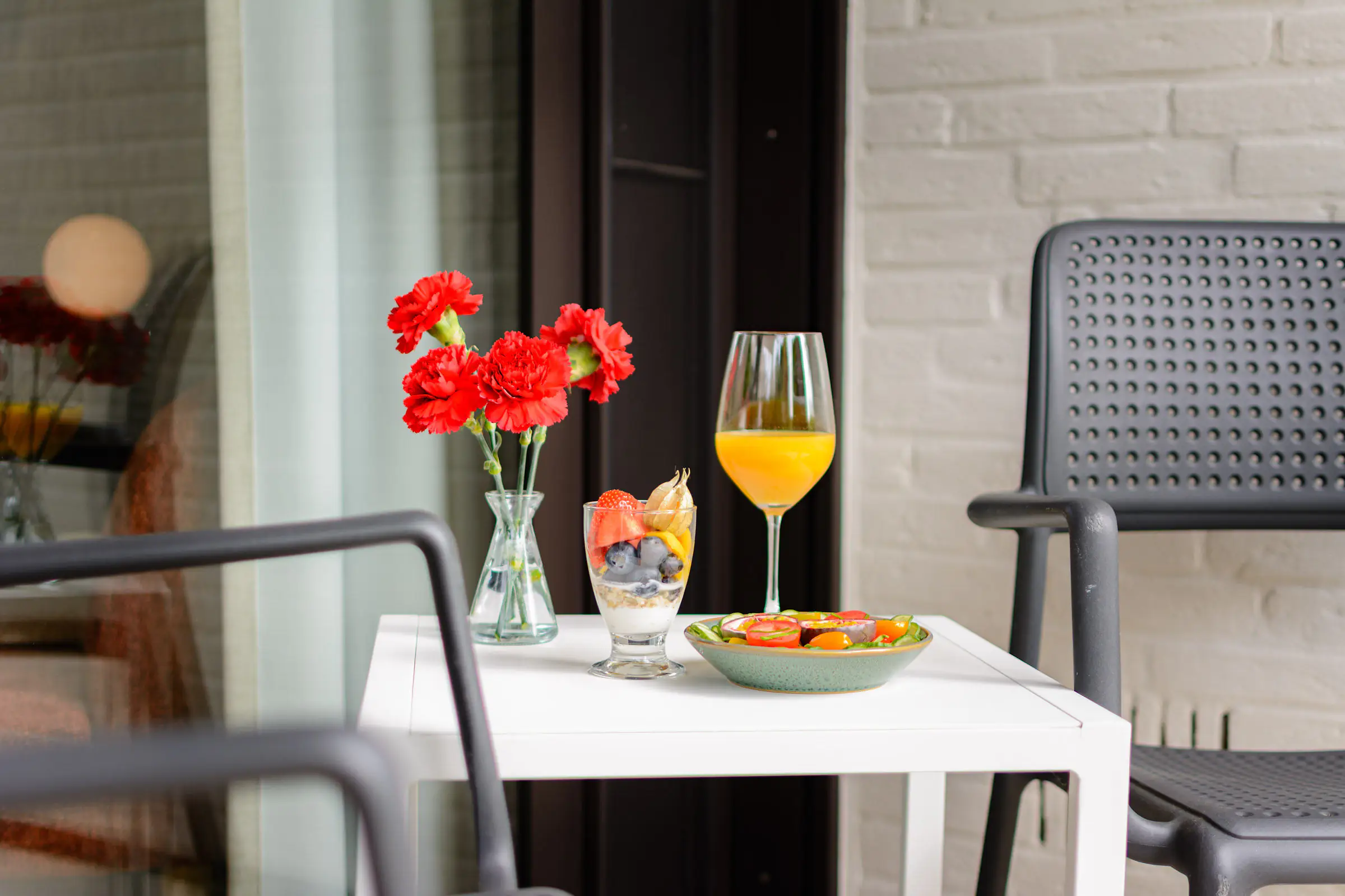 Ontbijt buiten op het terras met vers fruit, verse jus en rode anjers