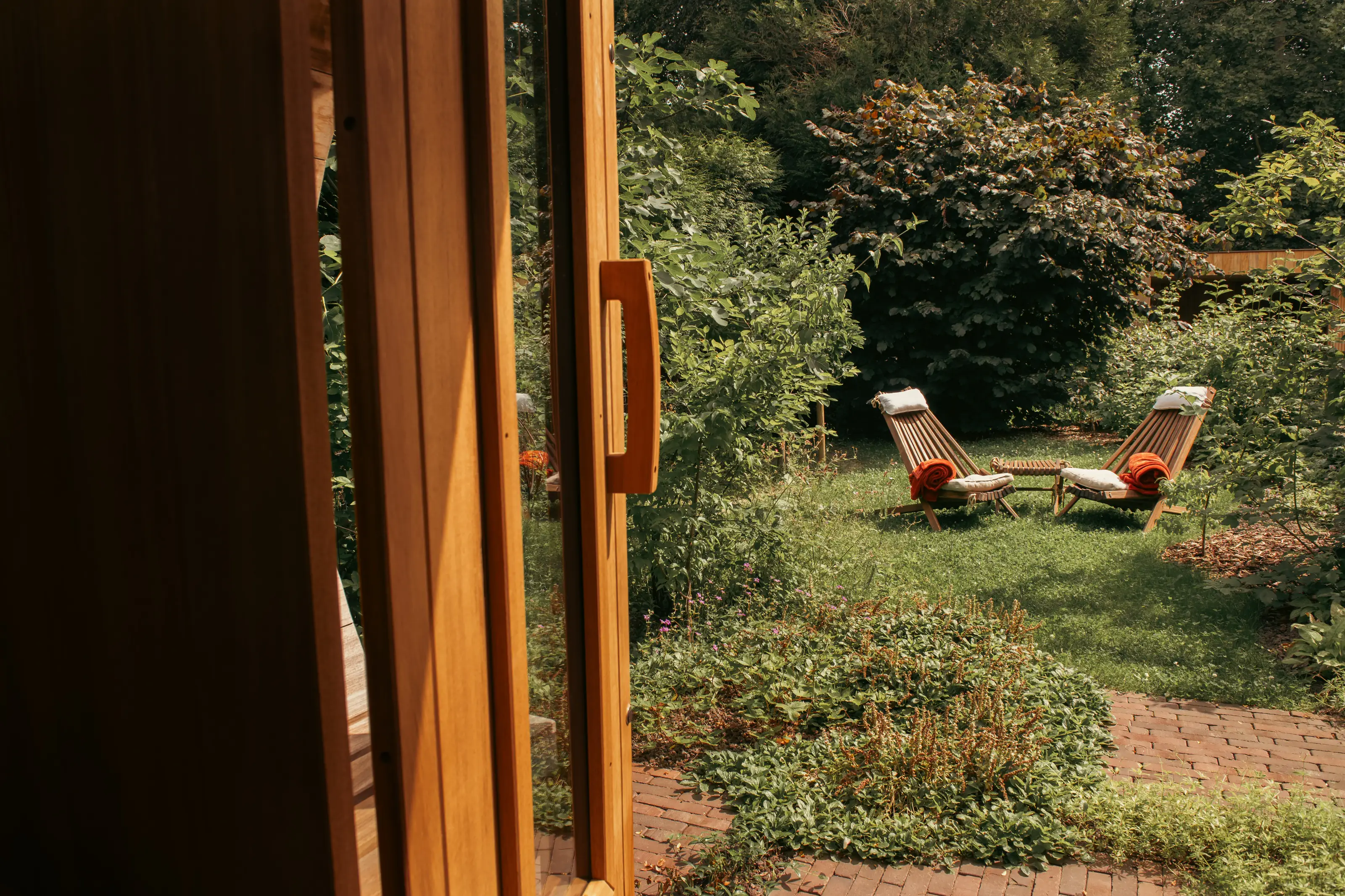 Zicht vanuit de sauna op ligstoelen in de groene tuin